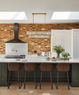 A kitchen with a large black island and range hood, and a red brick wall