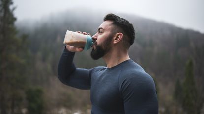 best weight gainer: Pictured here, a sportsman drinking protein in shaker bottle outdoor in front of foggy hill in autumn season, close up, drinking water after outdoor exercise.
