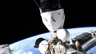 two white spacecraft are seen docked at different orientations on a space station, floating above Earth.