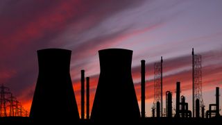 A photo of two cooling towers at a nuclear power plant, taken at sunset. The towers form silhouettes against the pink and blue sunset sky.