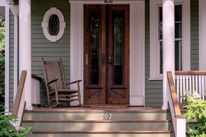 a small porch painted in pale green and white with a wood rocking chair