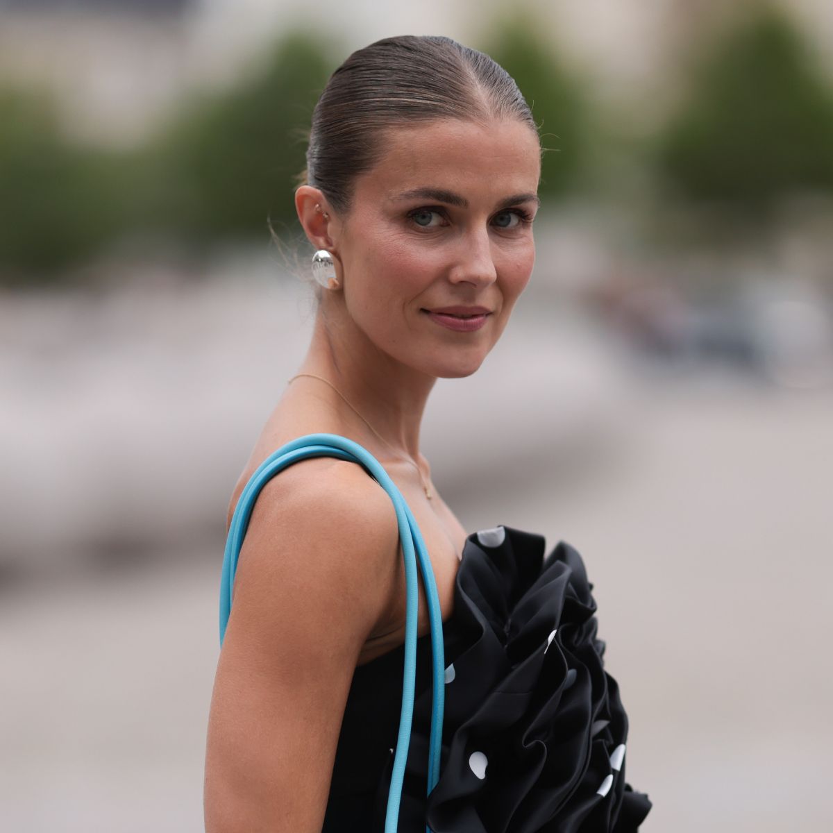 best bronzers for pale skin - woman with bronzed skin, slick back hair and a blue handbag
