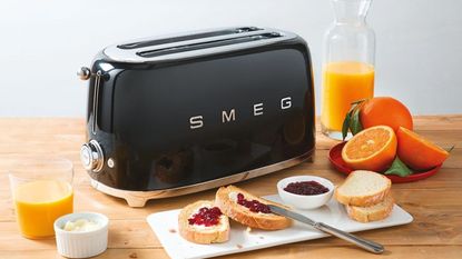 A Smeg 4 Slice Toaster TSF02 in black next to toast and orange juice