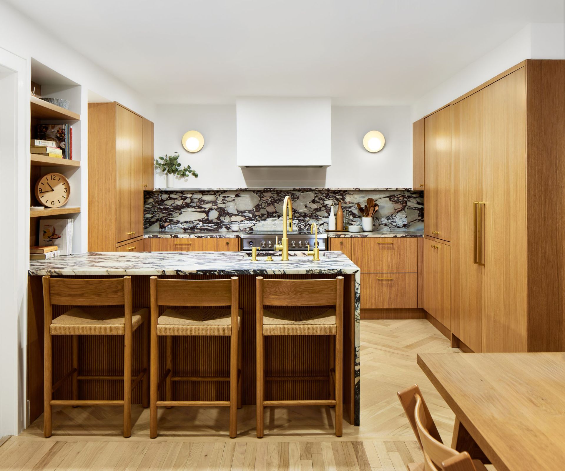 A kitchen with white oak cabinets, white oak flooring, and bold black and white marble countertops and backsplash