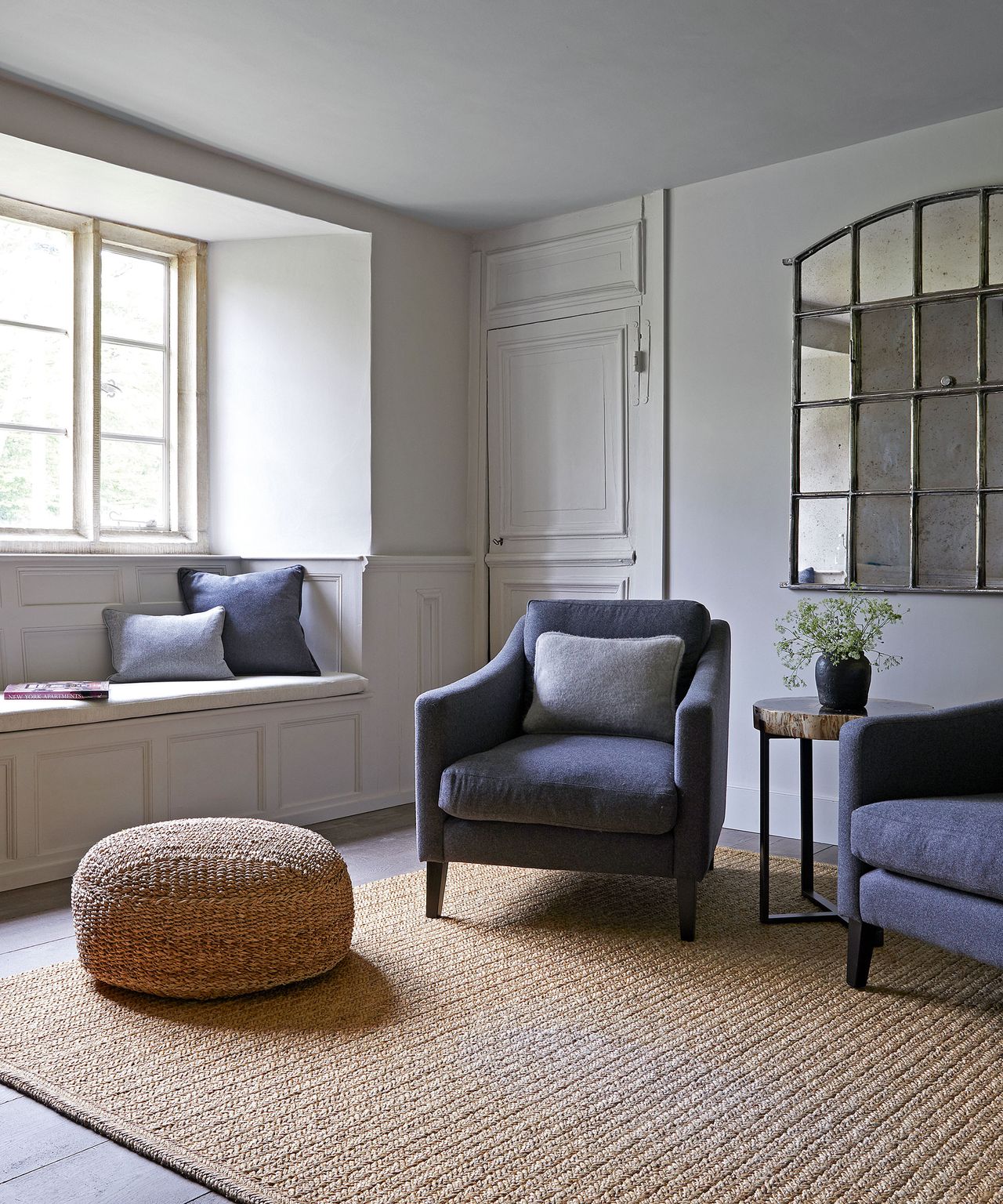 Neutral living room with window seat, gray armchair, benches and curved mirror