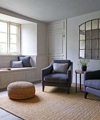 neutral living room with window seat, gray armchair, pouffe and arched mirror