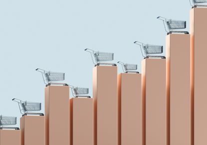 Digital generated image of vertical bar graph made out of golden cubic blocks with shopping carts standing on them against light blue background