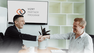 A Vizrt employee shaking hands with a smiling partner to kick off their partner program together. 