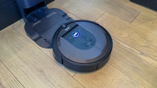 En svart Roomba i7 är på väg till sin laddningsstation som står på ett ljust träfärgat golv.