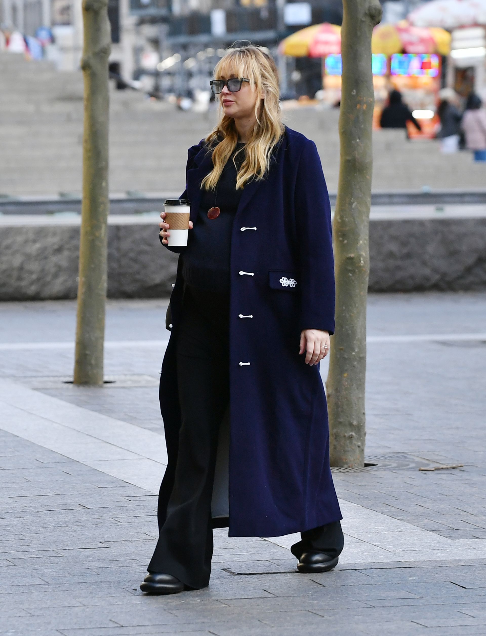 Jennifer Lawrence in New York City wearing a long navy-blue coat with black trousers, sunglasses, and flat shoes.