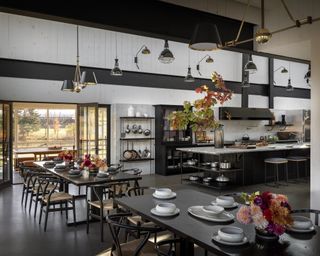 Kitchen lighting ideas with black pendants, gold two-buld chandeliers with black lampshades and brass wall sconces in a monochrome converted barn kitchen