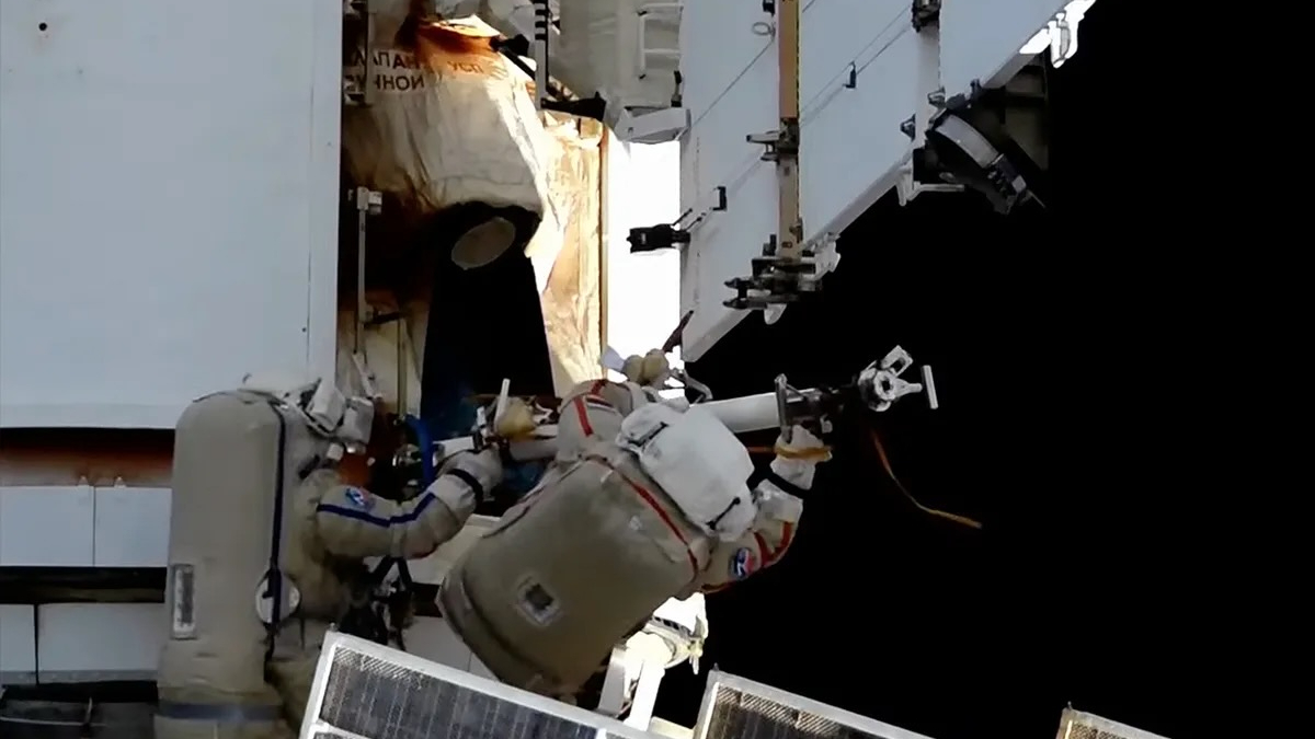two astronauts in white spacesuits work outside the international space station