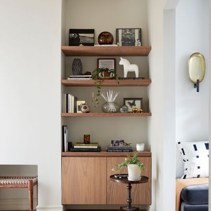 Three wooden shelves in an alcove with books and pictures on them, above a wooden sideboard