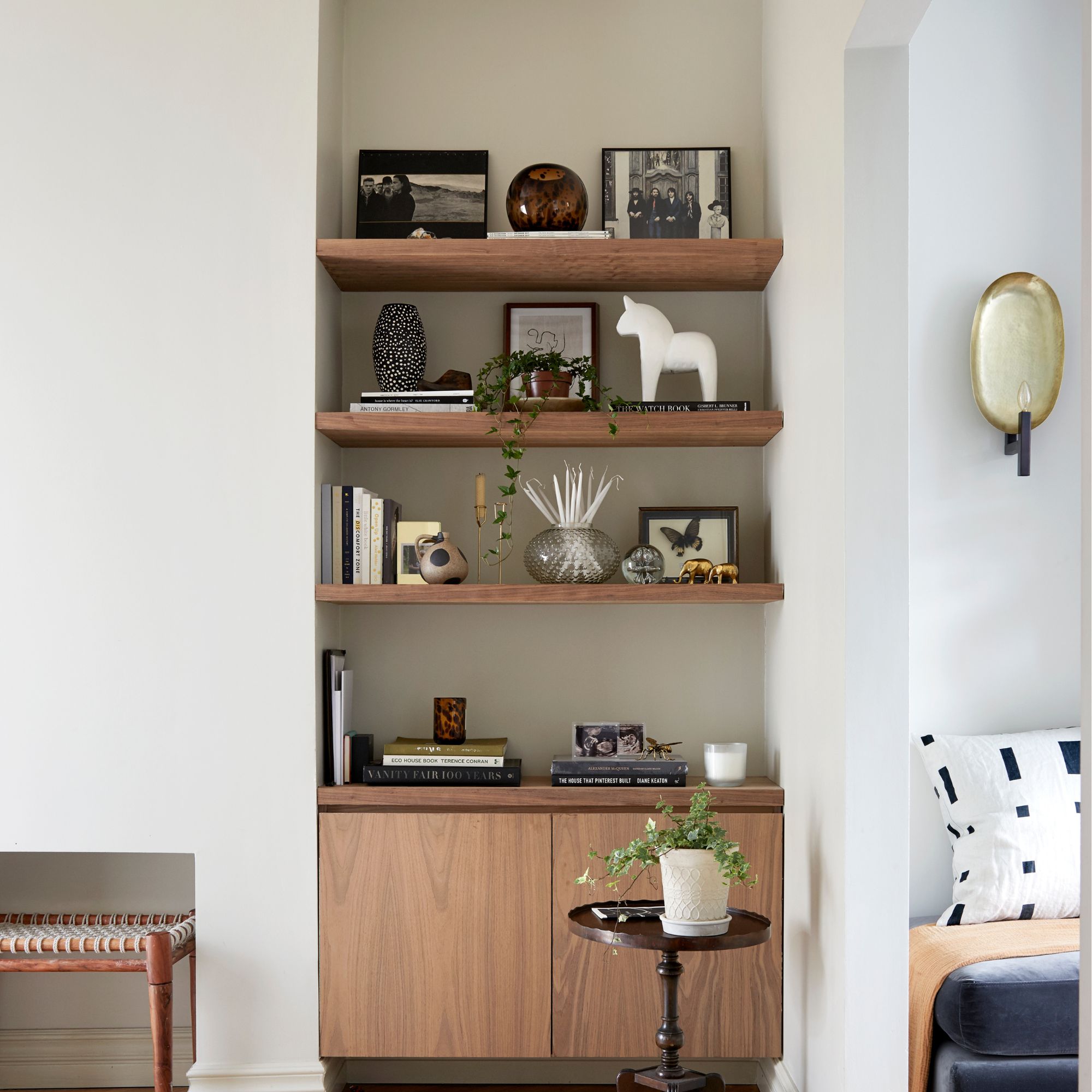 Three wooden shelves in an alcove with books and pictures on them, above a wooden sideboard