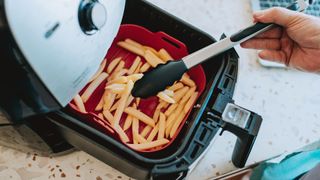 picture of man using liner and tongs to cook chips in air fryer