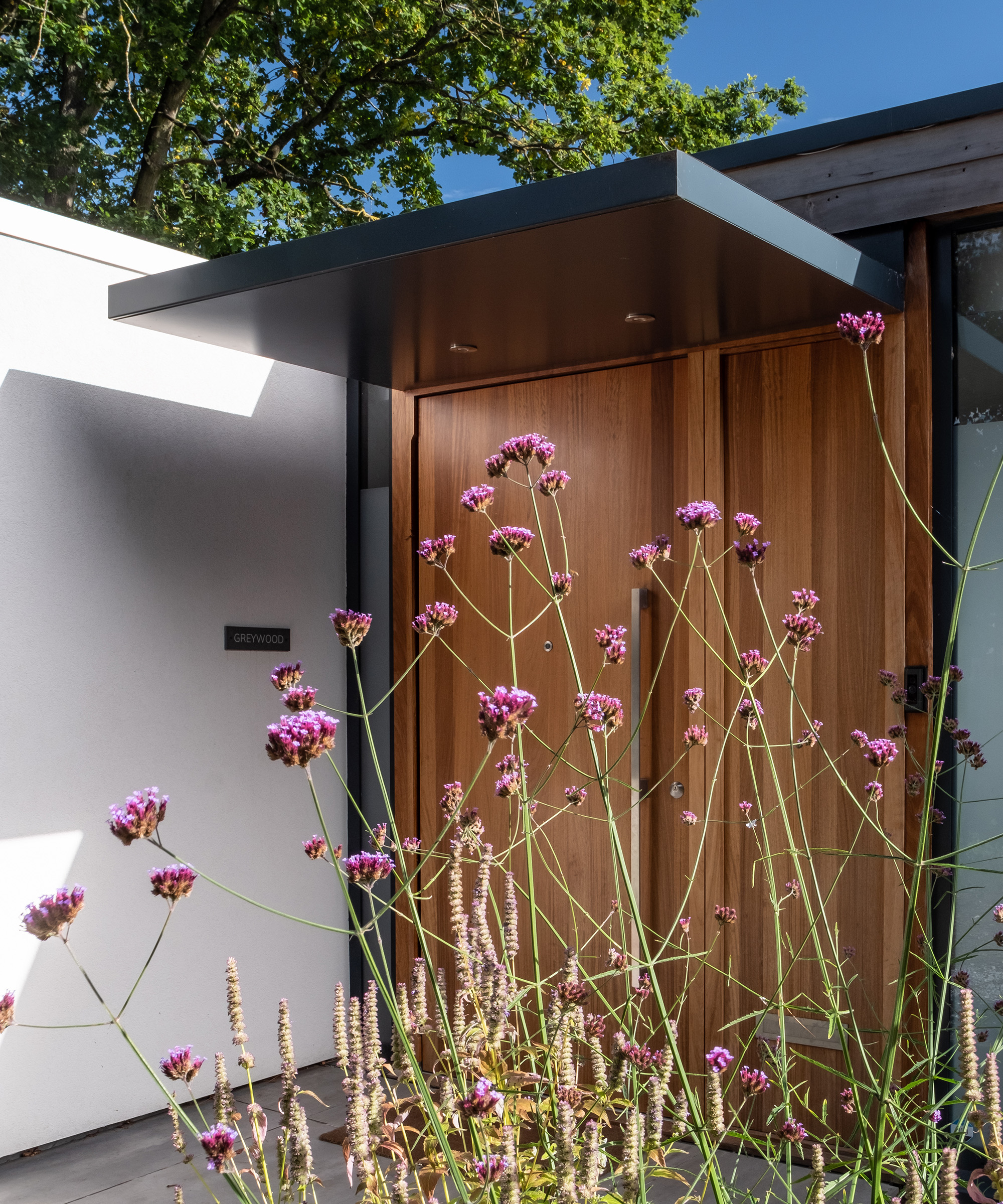 A modern timber front door of a self build home with some flowering herbs in front of the door