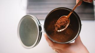 coffee grounds being scooped out of a jar with a teaspoon
