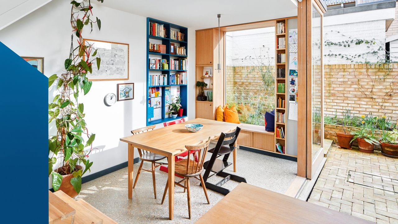 Kitchen-diner extension with wood table and chairs, window seat, blue built-in storage, concrete floor, sliding doors