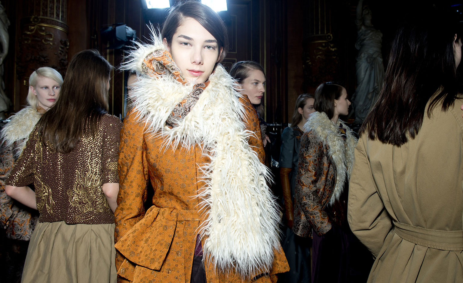 Woman wearing an orange coat with white fur scarf. People in the background