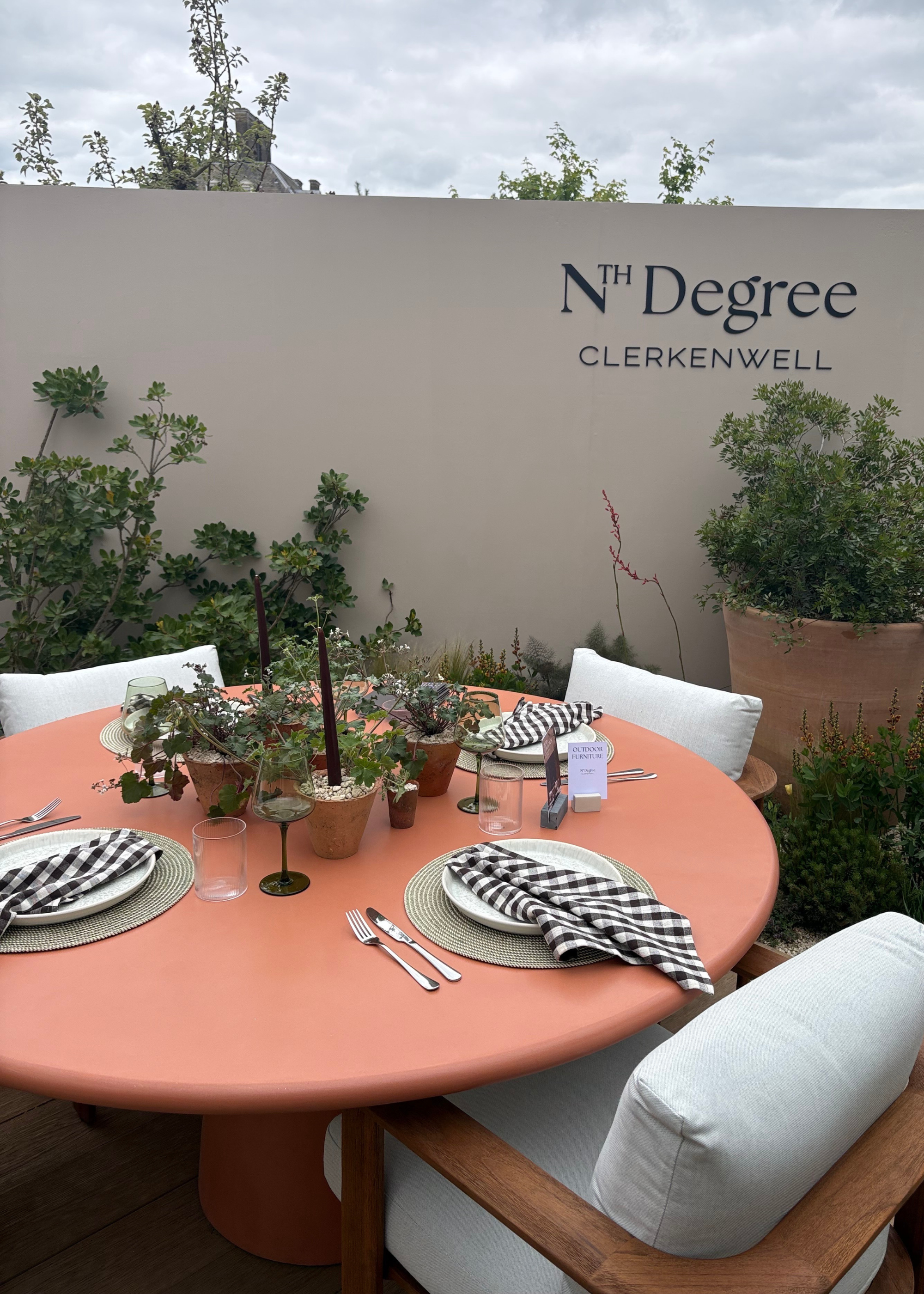 An outdoor space at the Chelsea Flower Show featuring Mediterranean garden design with a terracotta-colored dining table