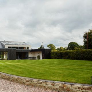 Large green grass lawn in front of house surrounded by stone brick edging in garden