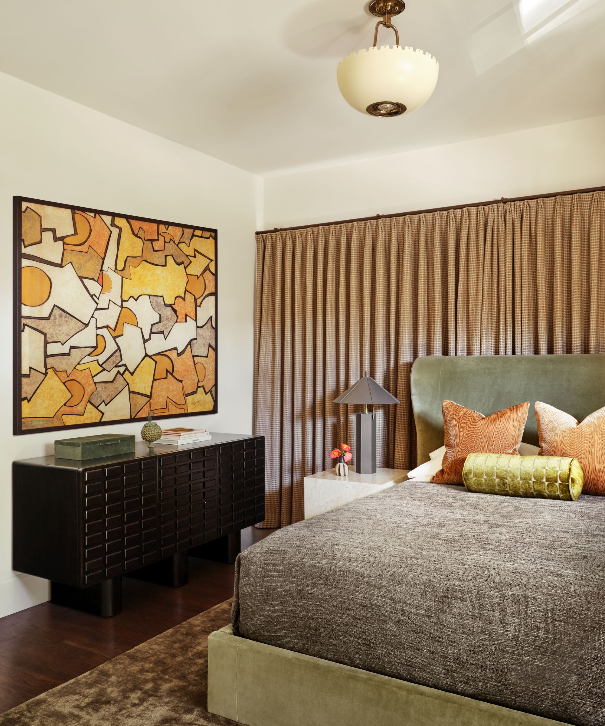 Bedroom with warm colors, modern art, orange and green throw cushions, dark wood floor and curtain rail