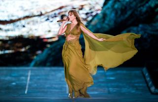 Taylor Swift wears a green alberta ferretti dress with a stomach cut out and a sheer cape while performing on the eras tour