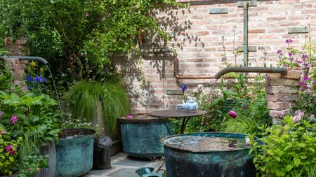 Courtyard garden with water pipes flowing into large blue copper pots and lush, cottage-style planting