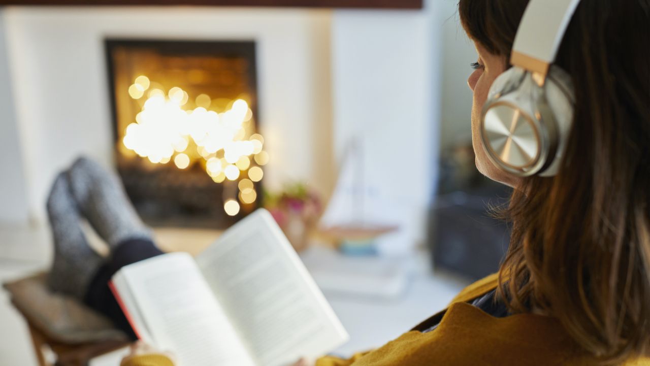 Woman with headphones reading in living room - stock photo