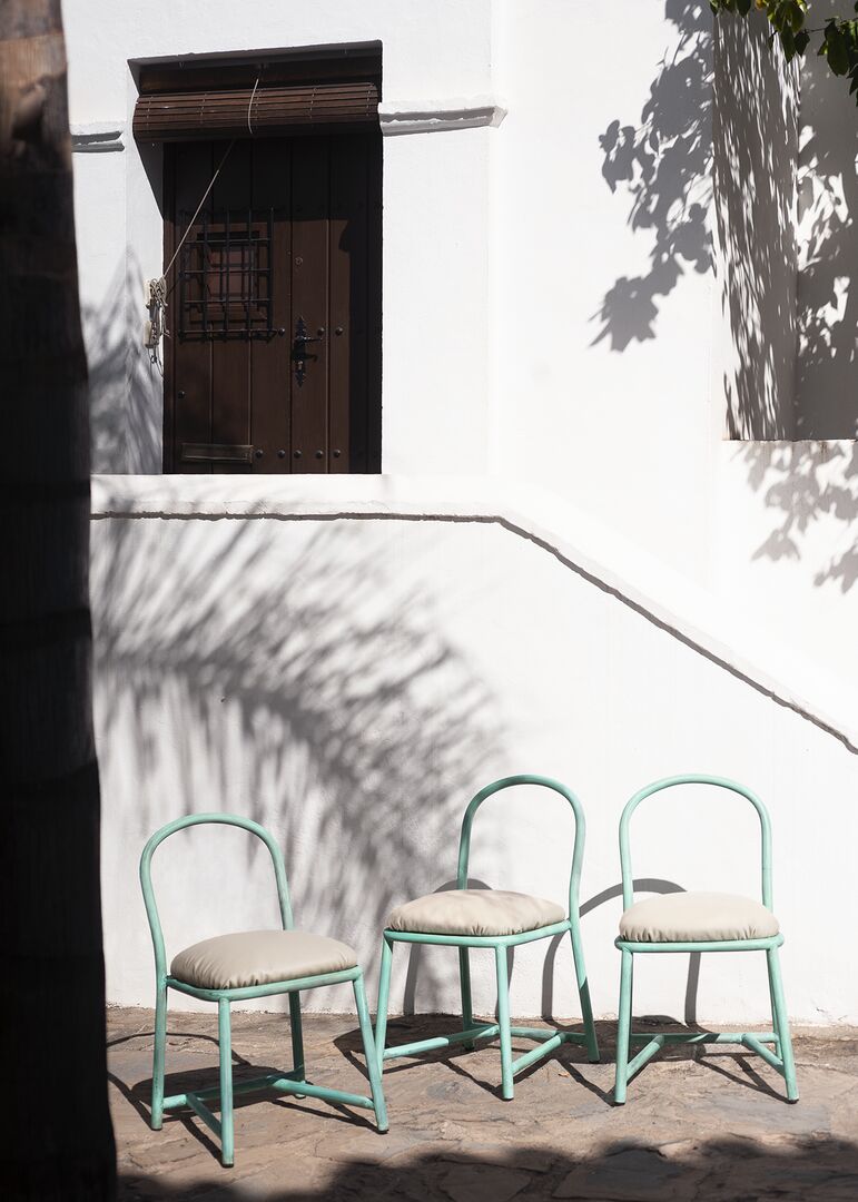 three green tubular steel frame chairs sit in front of a stairwell with palm leaf shadows