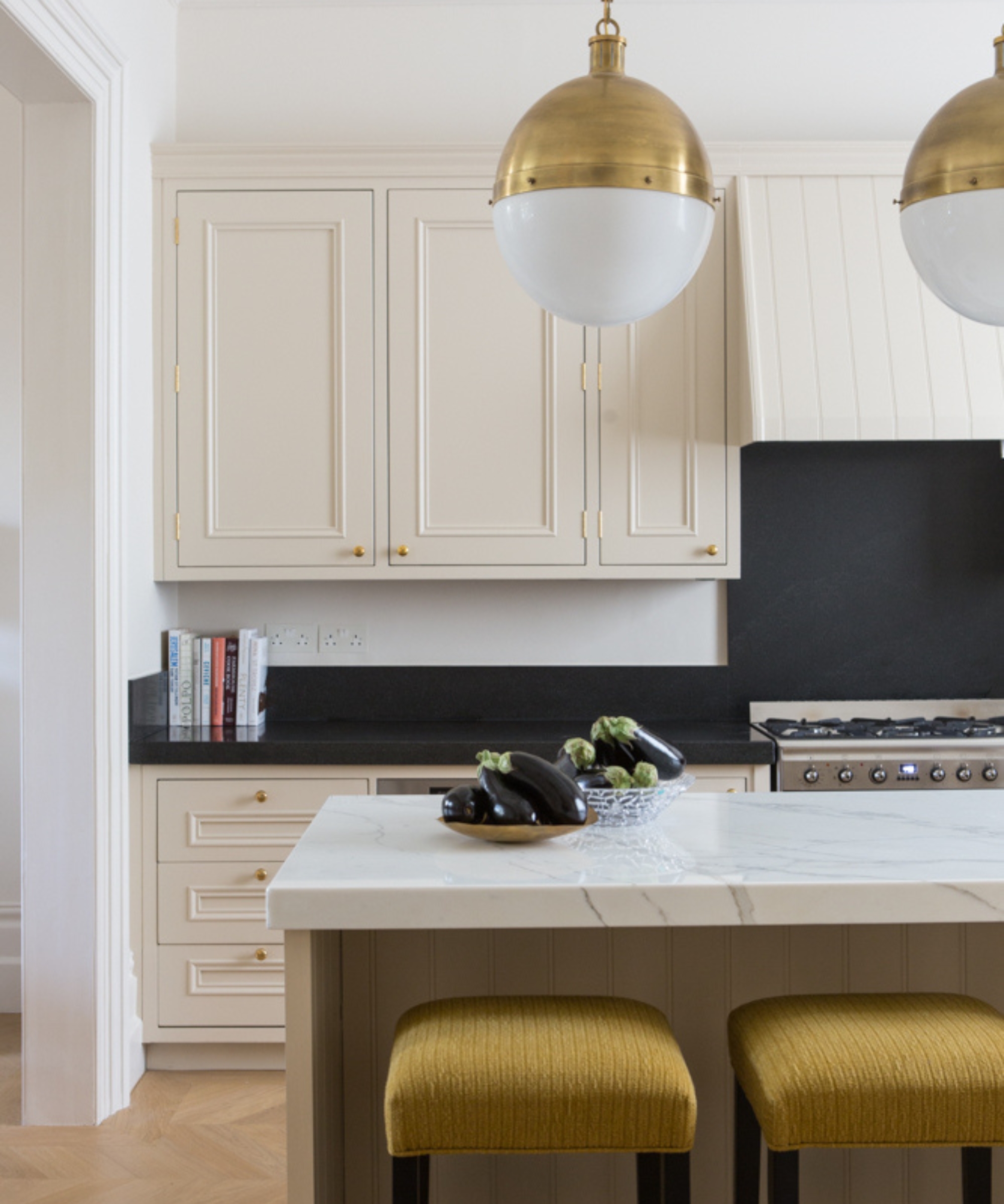 A warm white kitchen with black countertops, brass hardware, and decorative molding on the cabinets
