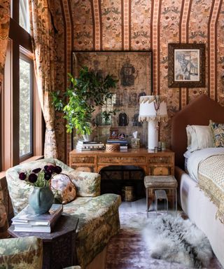 House of Hackney collection with Pierce and Ward - bold patterned chair, wallpaper, and curtains beside a bed with a chest of drawers as a bedside table. a patterned lamp on top