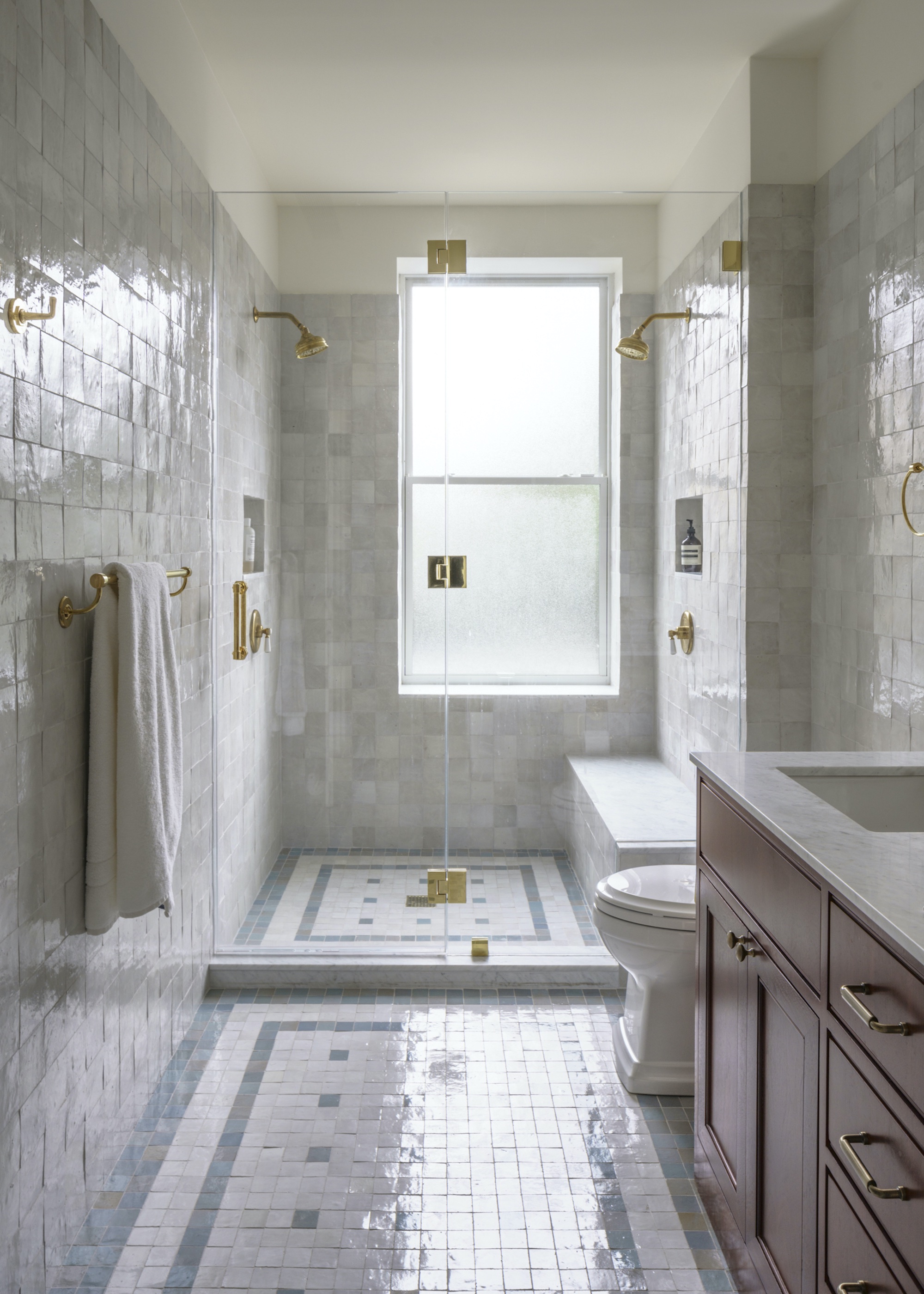 bathroom with tiling on the floor and walls. There is also a shower in the bathroom with glass doors as well as a sink with drawers and cabinets