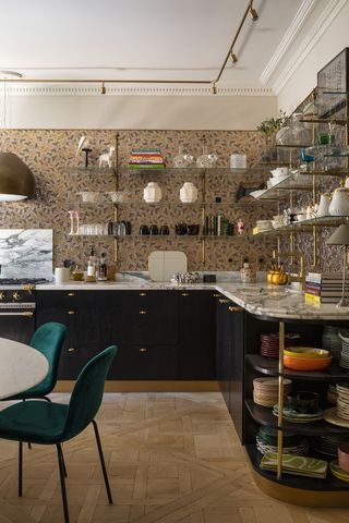 A large kitchen with L shaped black cabinets with marble counters and gold shelving