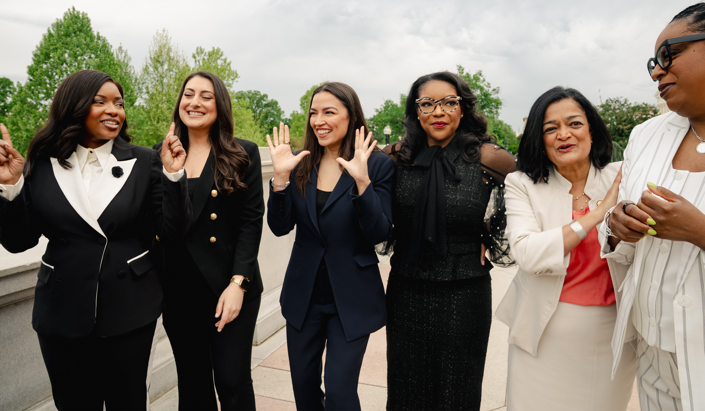 Several congresswomen laugh and gesture between takes on the Capitol grounds. From left: Jasmine Crockett, Sara Jacobs, Alexandria Ocasio-Cortez, Emilia Sykes, Pramila Jayapal, and LaMonica McIver.