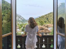 A mature woman rests on a balcony looking at a mountain view. She appears to be in her 40s.