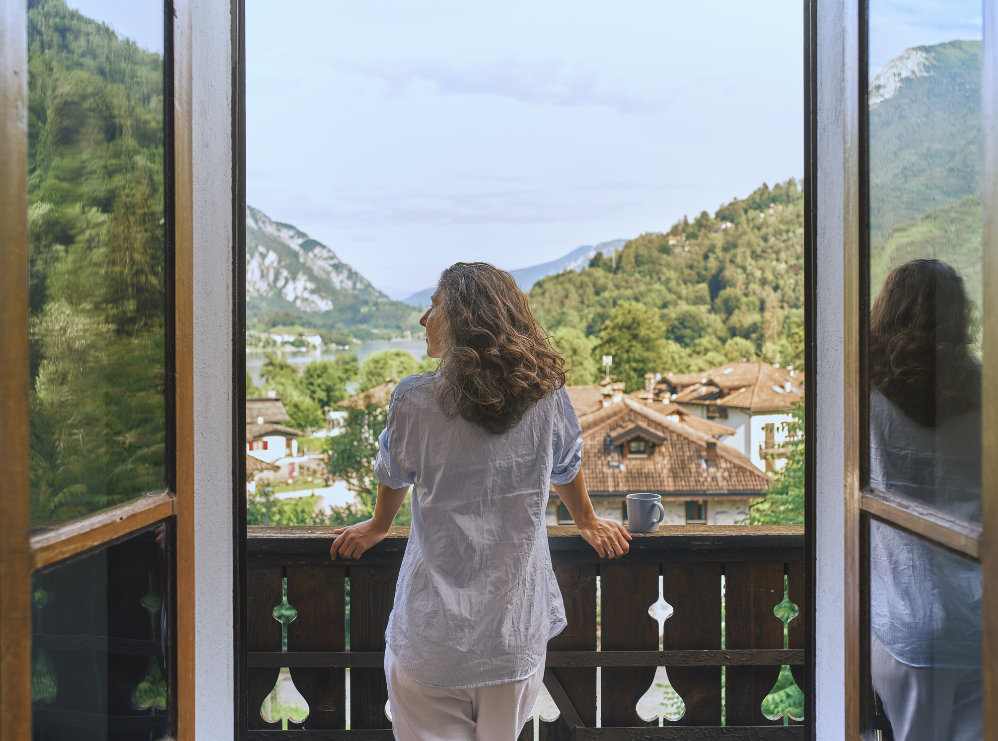 A mature woman rests on a balcony looking at a mountain view. She appears to be in her 40s.