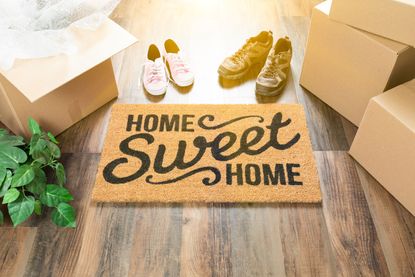 Doormat that says "Home Sweet Home" surrounded by boxes, and two pair of shoes