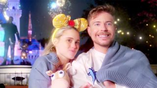 Mr/ Beast and his fiance in a sweater and holding a stuffed animal at Disneyland after hours in front of the castle.