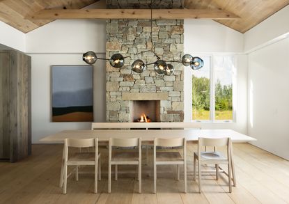A wooden dining table next to a brick fireplace and lit fire