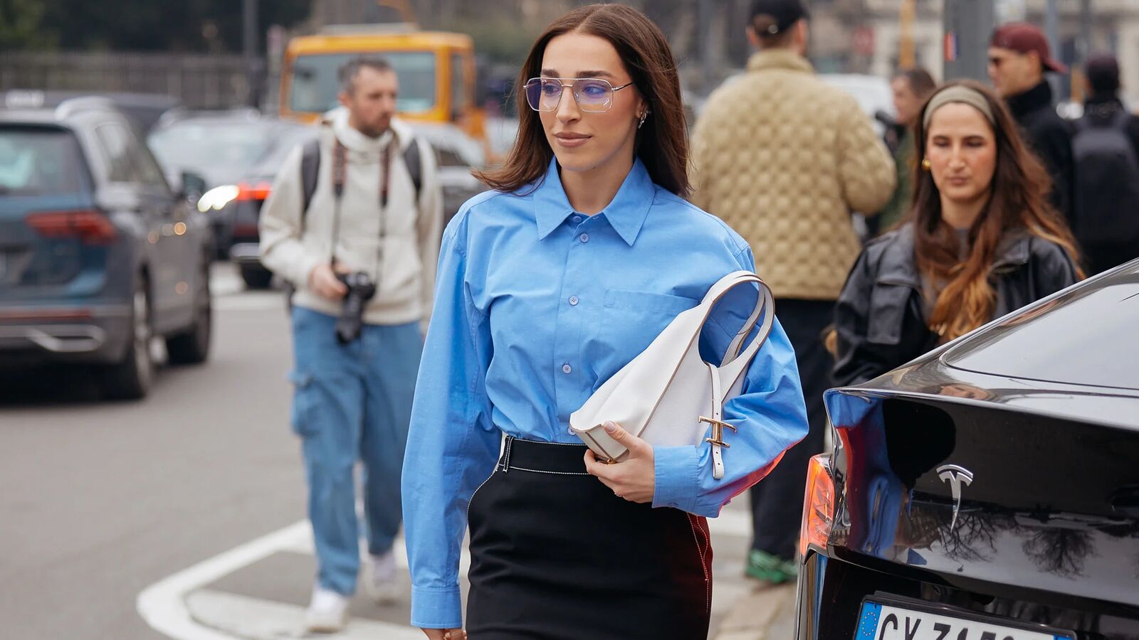 Woman wears button down, black pencil skirt, white handbag, and black heels.