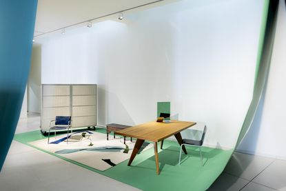 A museum display with green background showing furniture curated by Muller Van Severen