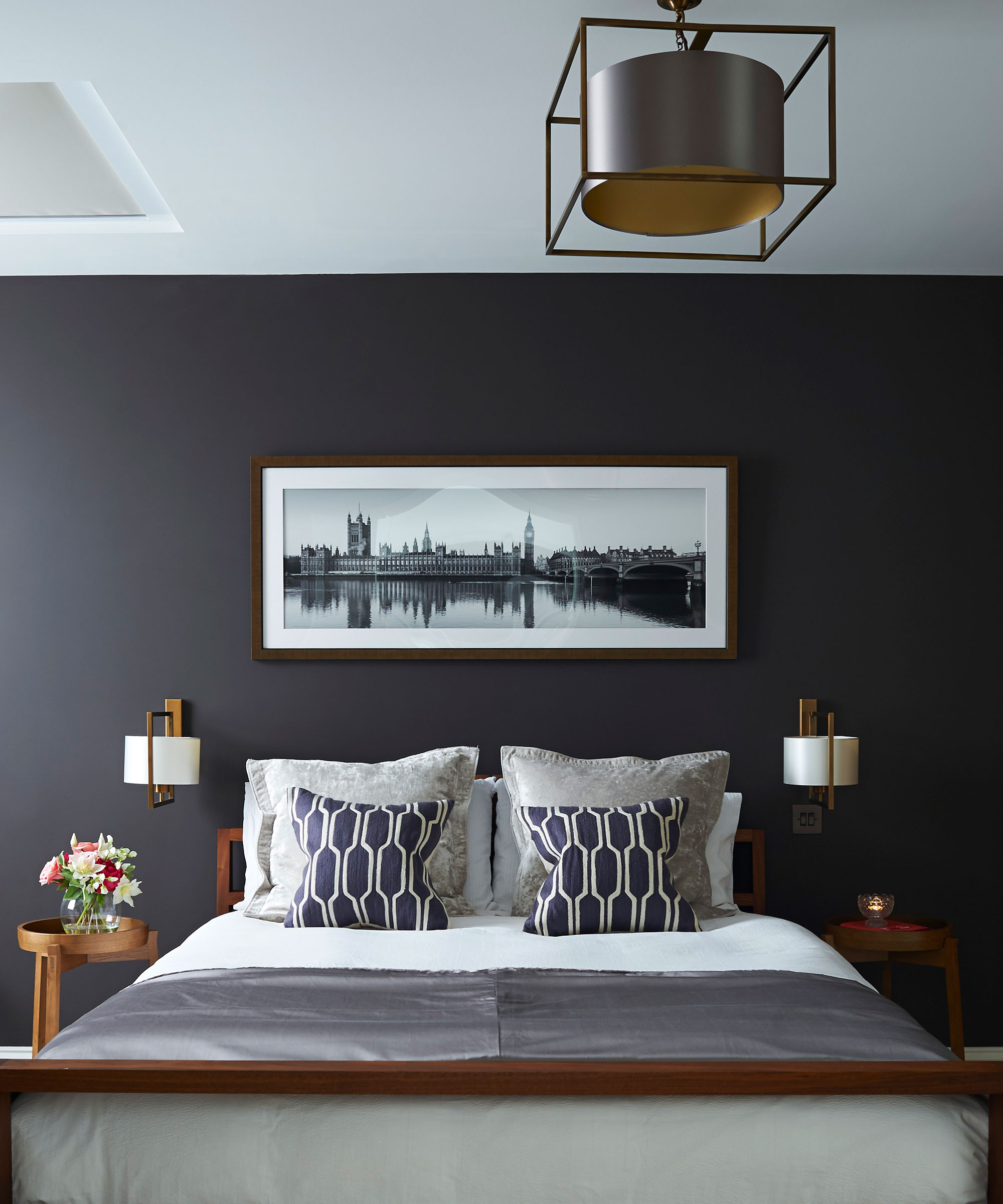 An example of bedroom lighting ideas showing a dark gray wall behind a bed with white and gray bedding and white wall lighting