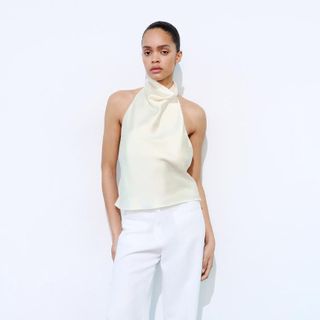 Model wearing cream halterneck top and white trousers