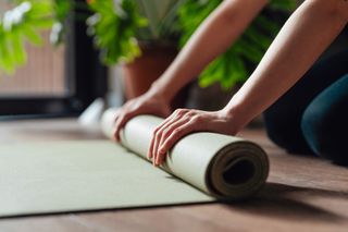 A close up of a person unrolling their yoga mat in their home.