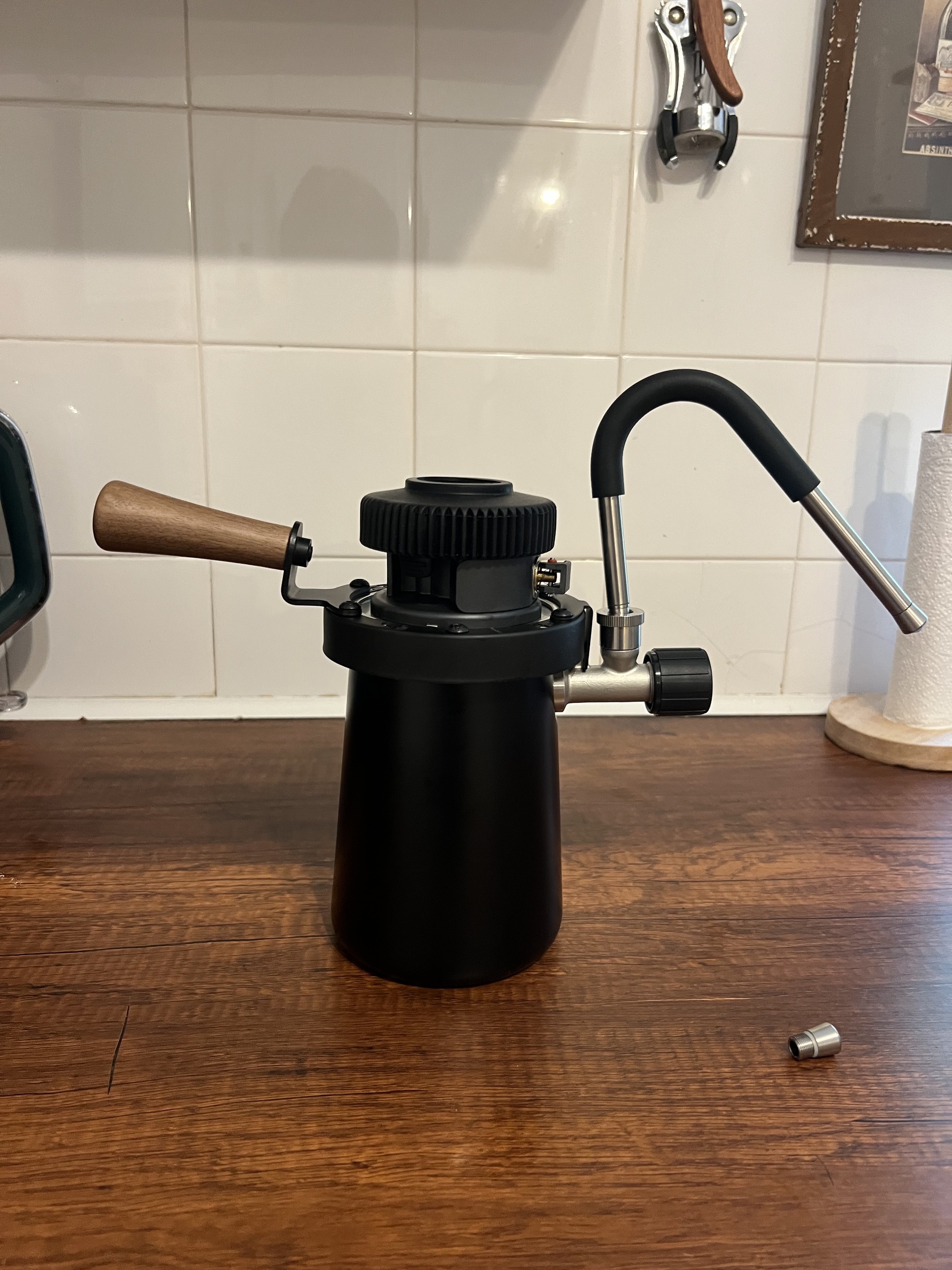 Image of a black stovetop milk steamer with a wooden handle on a wooden countertop.