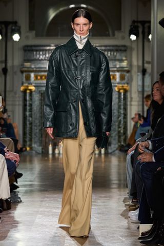 A FW24 Victoria Beckham model wearing a green coated barn jacket with khaki pants.