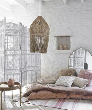 Relaxed boho space with intricate, white-wash room divider, natural ceiling pendant, and variety of floor cushions in mixed, tactile designs.