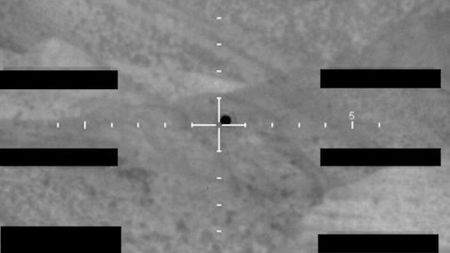 a dark blob seen against a mountainous desert landscape in a monochromatic, grainy photograph
