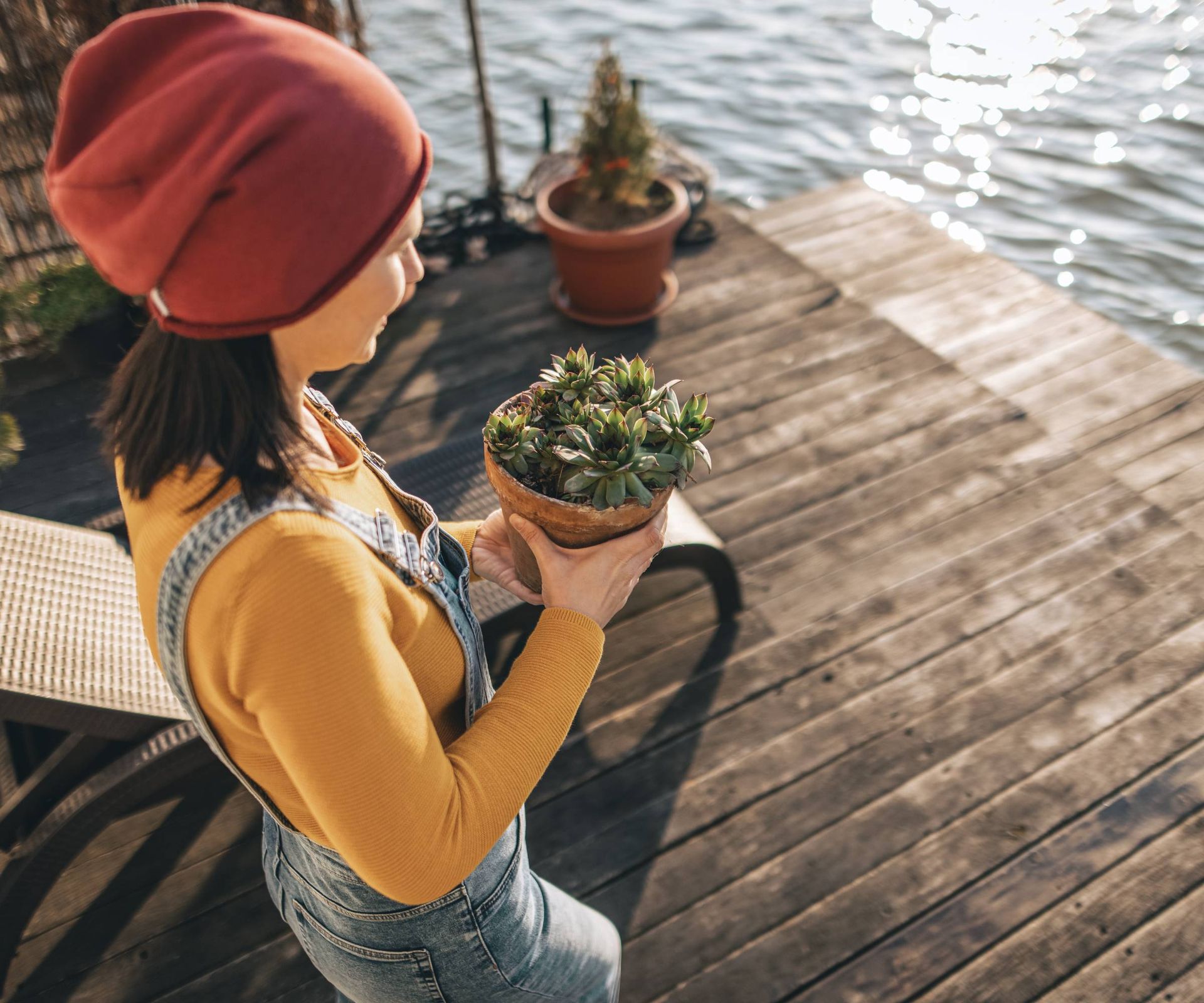 A woman in a winter hat carries a potted succulent onto a dock